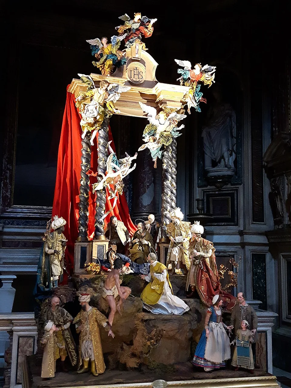 Presepe monumentale con baldacchino dorato e drappo rosso allestito in una chiesa